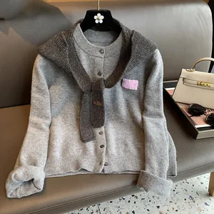 Close-up of gray knit cardigan with wool texture and pink decorative patch on a leather sofa