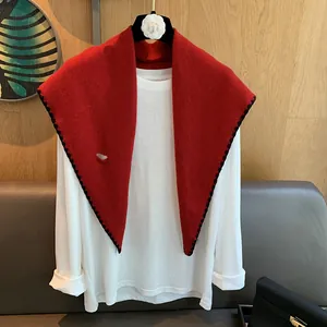Détail d'un châle rouge en pure laine avec bordure festonnée noire sur un haut blanc