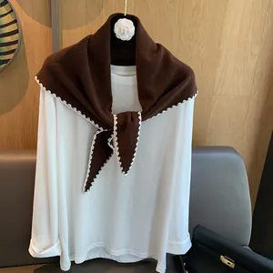 Détail d'un châle en laine marron avec bordures festonnées blanches sur t-shirt blanc