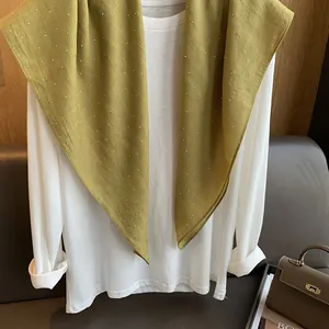 Détail d'une écharpe vert olive à strass avec tissu texturé sur une chemise blanche