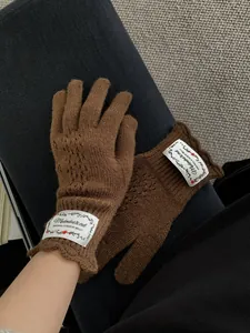 Macro view of brown knit gloves with intricate hollow patterns and branded woven label