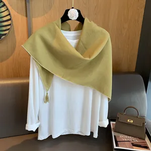 Detail eines hellgrünen Baumwoll-Leinen-Schals mit Quasten auf weißem Outfit