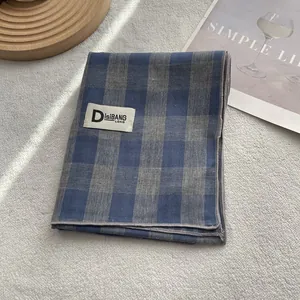 Detailed close-up of blue plaid cotton scarf with fine stitching and brand woven label