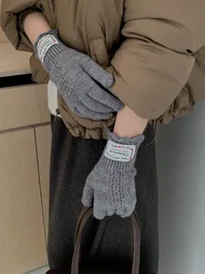 Detail of grey knitted gloves featuring lace hollow patterns and woven fabric labels