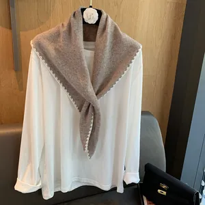 Détail du bord du châle en laine avec couture festonnée blanche sur tissu beige