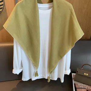 Detail eines senfgelben Leinenschals mit Quasten über einem weißen Langarmshirt