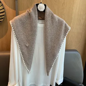 Gros plan détaillé d'une écharpe en laine beige avec bords ondulés et logo métallique