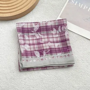 Close-up of purple plaid silk scarf with white leaf prints on a soft textured background