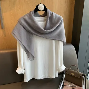 Gros plan sur une écharpe en coton et lin gris ornée de strass sur un t-shirt blanc à manches longues