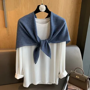Détail d'une écharpe en coton bleu foncé à pois nouée sur un haut blanc à manches longues