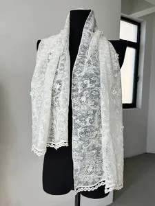 Detailed macro view of white lace scarf with intricate floral embroidery and hollow edges