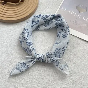 Detail view of light blue floral silk scarf knotted on a white textured fabric background