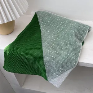 Detail of green pleated fabric joined with white polka dot mesh on a long scarf