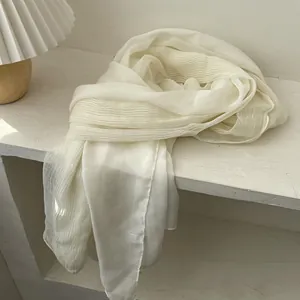 Detailed close-up of cream white pleated scarf texture with fine stitching and care label