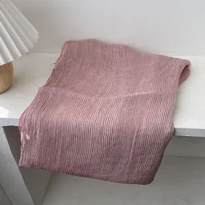 Detail of pleated pink ombré scarf showing textured vertical folds on a white table