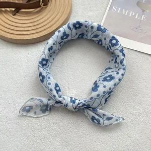 Detailed view of lightweight blue floral silk scarf tied in a knot on soft white texture