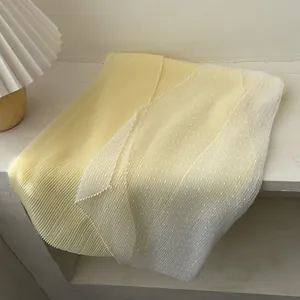 Detailed view of the yellow pleated fabric paired with white polka dot mesh on the scarf