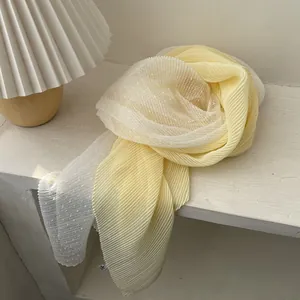 Detail of light yellow pleated scarf with white polka dot sheer fabric on a table