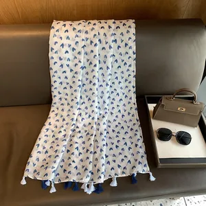 Elegant white cotton linen scarf with blue heart print and fringe tassels on a leather bench