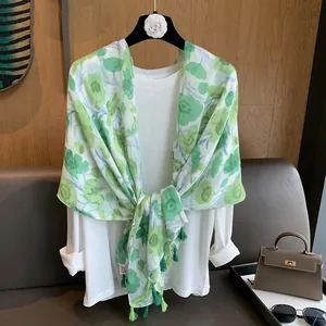 Détail d'une écharpe florale légère avec des glands verts sur une chemise blanche