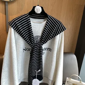 Detail of grey varsity sweatshirt with navy blue letters and striped knit shawl