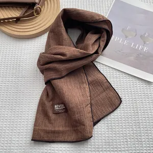 Détail d'une écharpe en coton marron foncé avec texture rayée et étiquette tissée