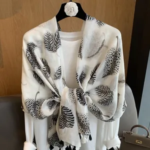 Detail of white cotton scarf featuring black leaf patterns and leopard print with tassels