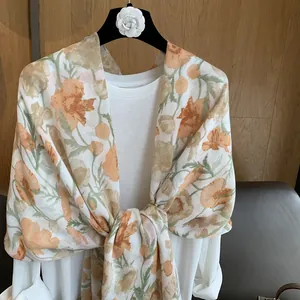 Détail d'un châle à fleurs orange et vert sur un tissu léger et respirant de qualité
