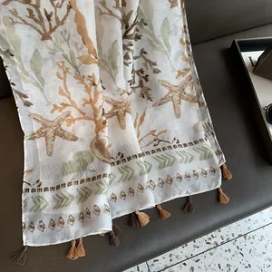 Detail of a lightweight linen scarf with sea coral prints and fringed tassels on a leather chair