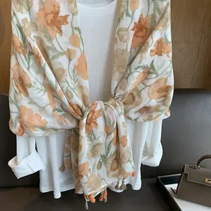 Détail d'une écharpe florale aux fleurs orange et franges élégantes sur chemise blanche