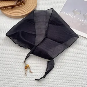Détail d'un foulard plissé noir avec perles en bois décoratives sur tissu blanc