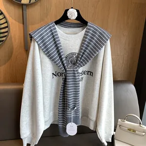 Detailed view of striped knit shawl layered over a grey sweatshirt with university print