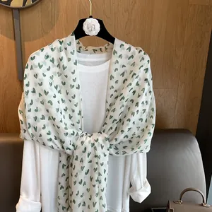 Detailed texture of white lightweight scarf featuring green heart prints and fringe