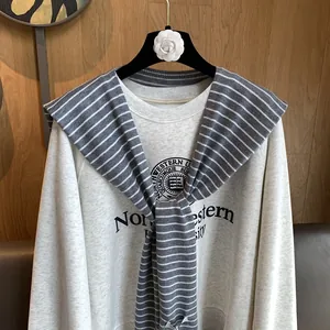 Detail view of a gray sweatshirt paired with a blue and white striped knit shawl accessory