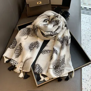 Close-up of white scarf with black leaf patterns and tassel detail on display