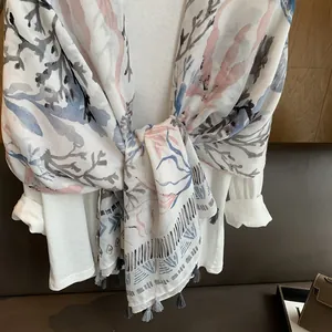 Close-up of coral print cotton linen scarf with grey fringe tassels on white shirt
