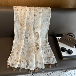 Detail of tropical palm leaf print scarf with fringe hanging on a leather sofa