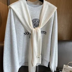 Detail of a beige knit shawl layered over a grey Northwestern University university sweatshirt