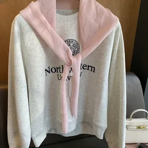 Détail d'un châle en maille rose à losanges superposé à un sweat-shirt gris collège