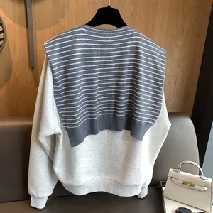 Detail of grey knitted sweater with striped vest overlay showing fabric texture