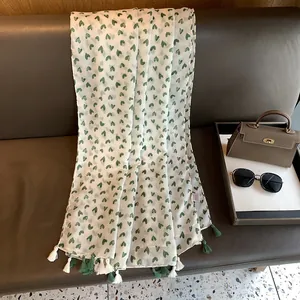 Detail of white cotton linen scarf with green heart prints and dual-tone tassels on a sofa
