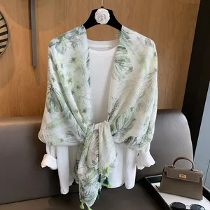 Detailed view of the tropical leaf print scarf with green tassel accents on a white shirt