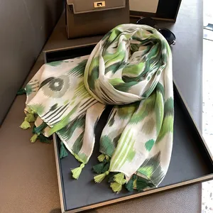 Artistic green and grey tie-dye scarf with tassel trim on a black tray with accessories