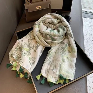 Detail of white scarf with tropical green leaves, elegant tassels and luxury accessories
