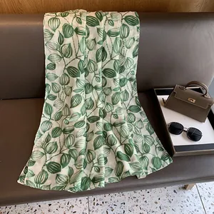 Dettaglio del motivo a foglie verdi con ricamo in seta dorata su un foulard di seta
