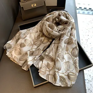 Dettaglio di sciarpa vintage con motivi di foglie in oro su tessuto bianco