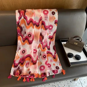 Detail of vibrant orange and pink bohemian headscarf with tassels on a grey leather surface