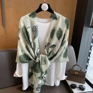 Detail of light green silk scarf with leaf prints and elegant tassel edges on a hanger