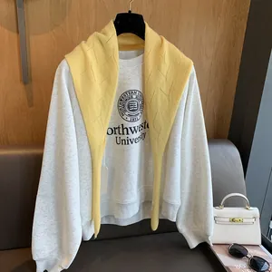 Détail d'un châle en laine jaune vif drapé sur un sweat-shirt gris avec logo d'université