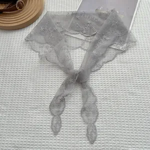 Détail d'une écharpe en dentelle grise avec broderie florale blanche et bord festonné